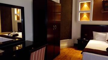 A hotel room with a large mirror, wardrobe, bedside table, and a bed with white linens.