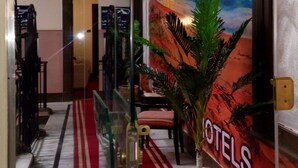 Eine Hotelhalle mit rotem Teppich, einer großen Wandmalerei mit Sonnenuntergang und einer Topfpflanze.