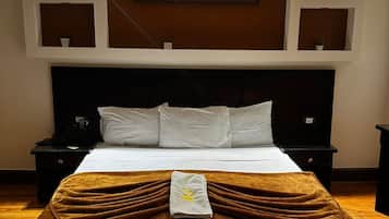 A hotel room with a large bed, a painting above the headboard, and wall-mounted sconces.