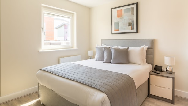 Une chambre à coucher bien rangée, avec un lit, des tables de chevet, une lampe et un tableau encadré au mur.
