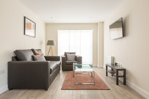 Una sala de estar moderna con un sofá gris, un sillón gris más pequeño, una mesa de centro de vidrio y una alfombra estampada.