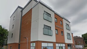 Un bâtiment moderne, identifiable grâce à une enseigne indiquant « Solstice House », qui se distingue par sa façade en briques, ses nombreuses fenêtres et son toit plat.
