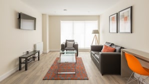 Un salon moderne avec une table basse en verre, un canapé, un bureau avec une chaise et une grande fenêtre.