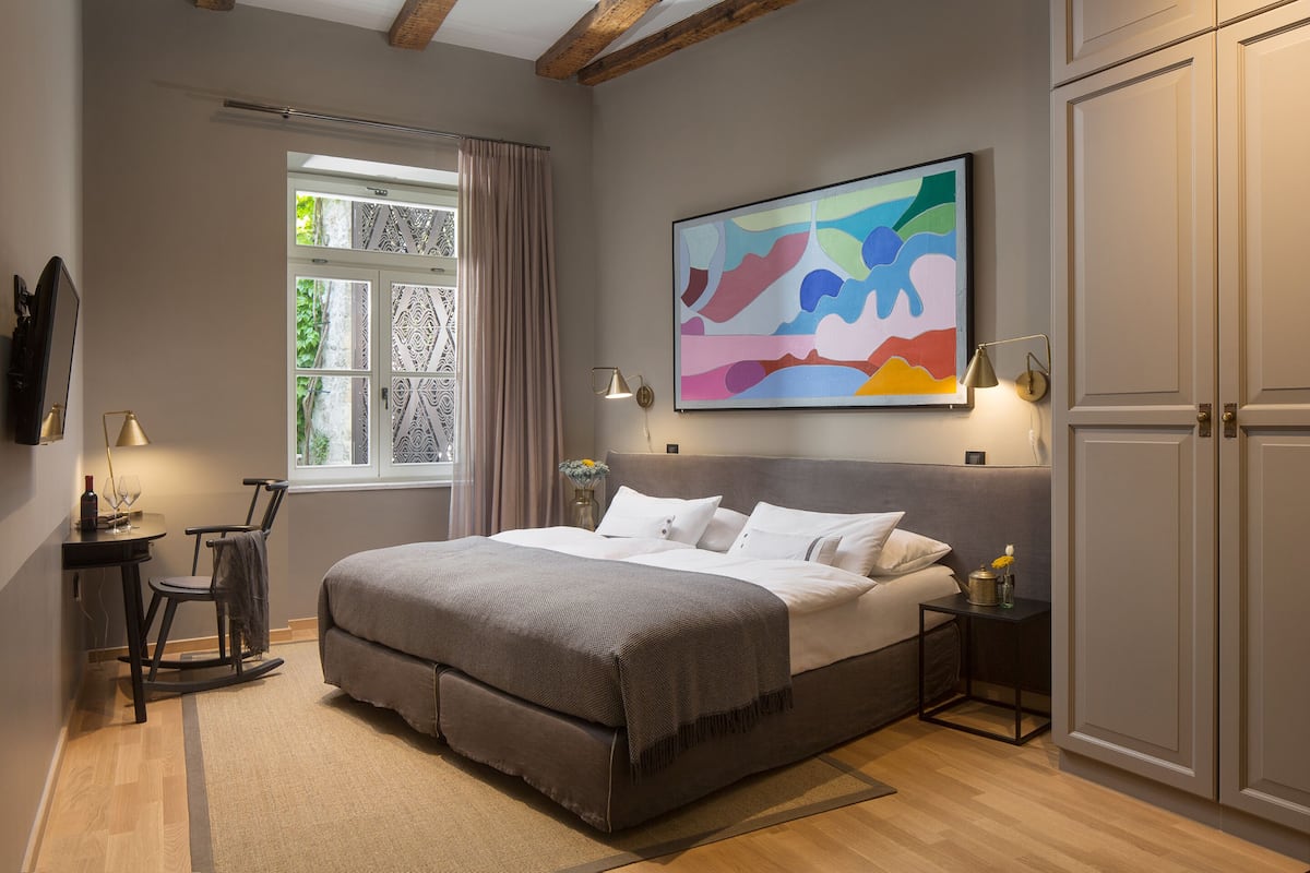 Une chambre à coucher comprenant un lit, un bureau, une chaise, une fenêtre avec des rideaux, un tableau et une armoire.