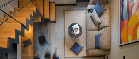 A modern interior with a staircase, a sofa set, a coffee table, and a colorful abstract painting.