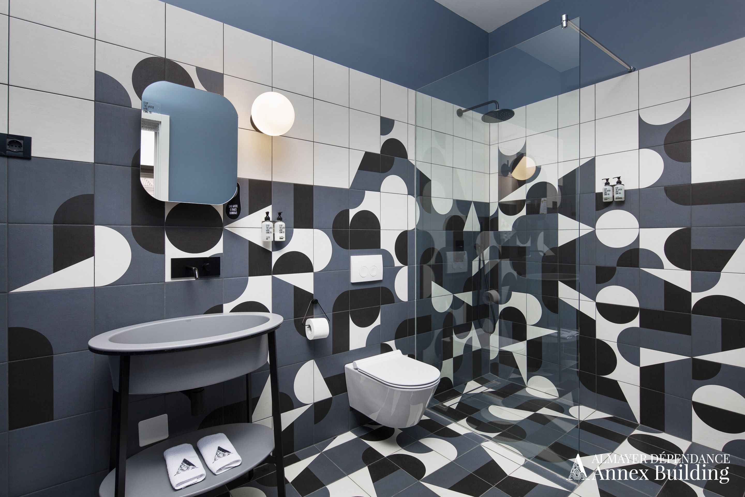 Un baño moderno con un estampado geométrico de azulejos, un espejo redondo, un lavamanos y un inodoro.