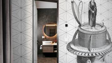 Een moderne badkamer met een geometrisch tegelpatroon, een ronde spiegel en een grote muurdecoratie.