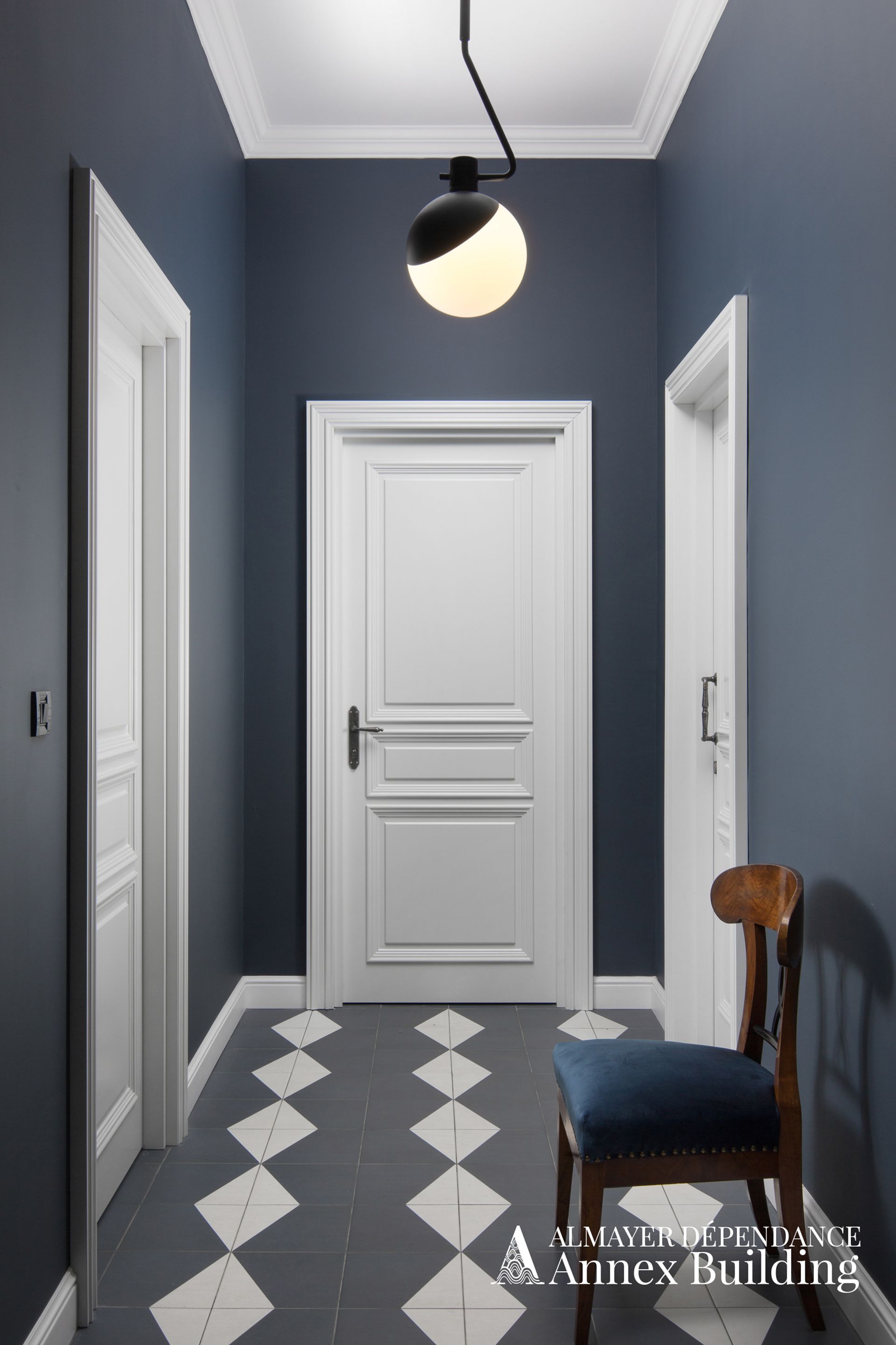 A hallway with a white door, a blue wall, and a patterned floor.