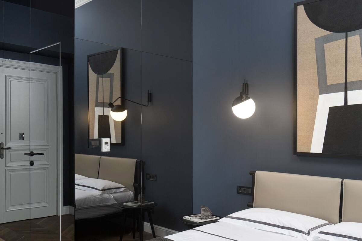 Une chambre à coucher moderne avec un grand lit, une table de chevet, une chaise et une lampe fixée au mur.