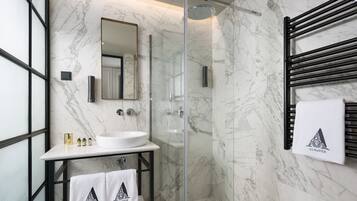 A modern bathroom with a marble wall, a glass-enclosed shower, a white sink, and black towel racks.
