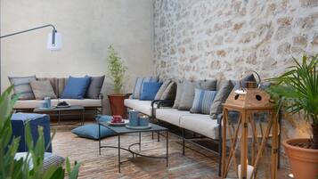 A cozy outdoor seating area with a stone wall, a wooden lantern, and a variety of cushions and a small table.