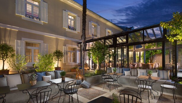 An outdoor seating area with tables and chairs, surrounded by potted plants and a building with large windows. - Almayer Art & Heritage Adults Only Hotel & Dépendance Rooms (Zadar)