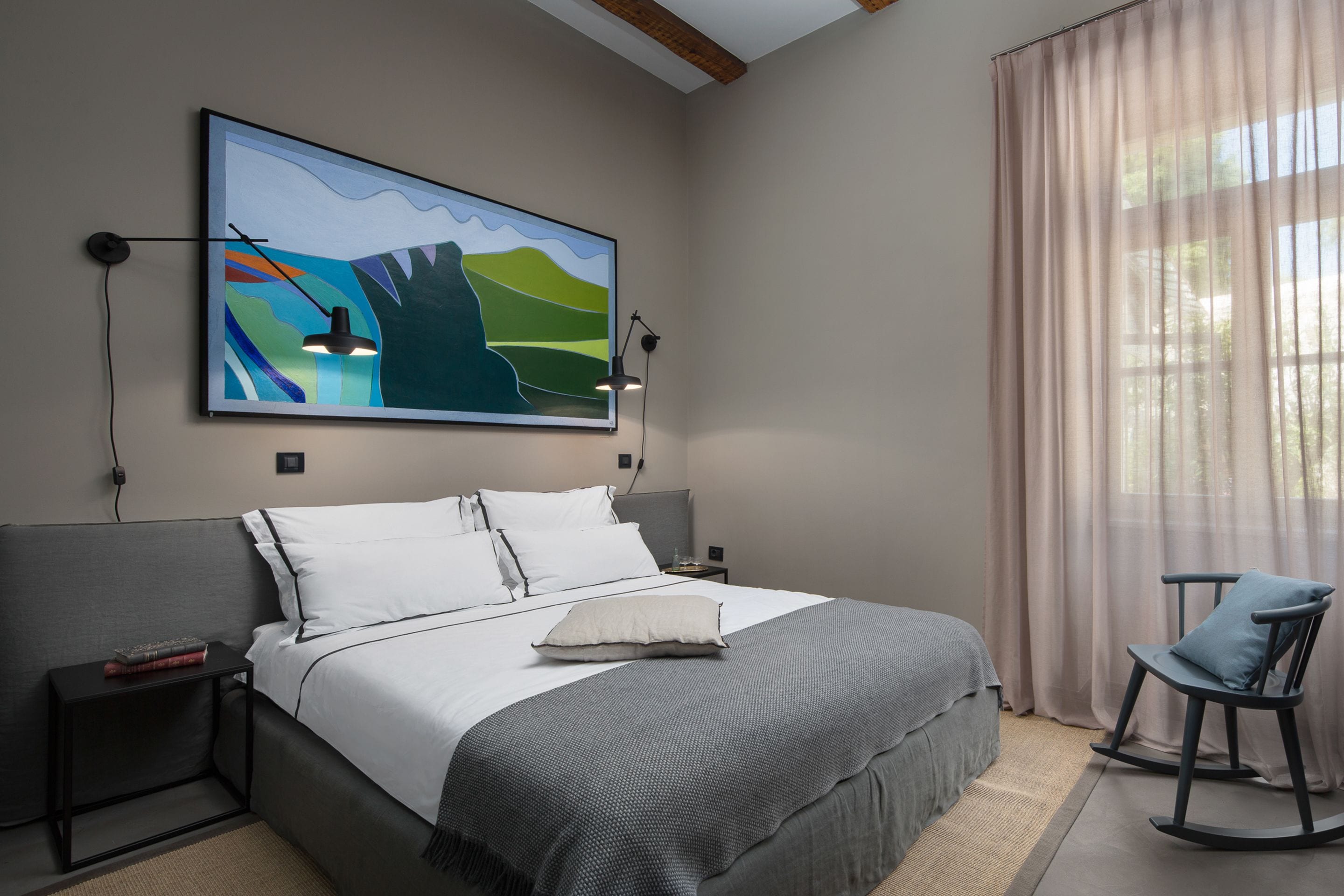 Un dormitorio moderno con una cama grande, un cuadro, dos mesitas de noche y una mecedora.