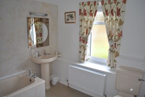A bathroom with a bathtub, sink, toilet, and window with floral curtains. - Airds Farm Guest House (Castle Douglas)
