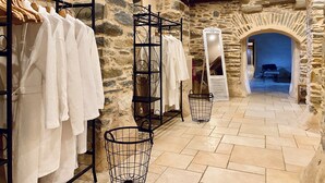 A stone-walled hallway with a rack of white robes, a mirror, and a basket. - Château de la Roque (Thereval)