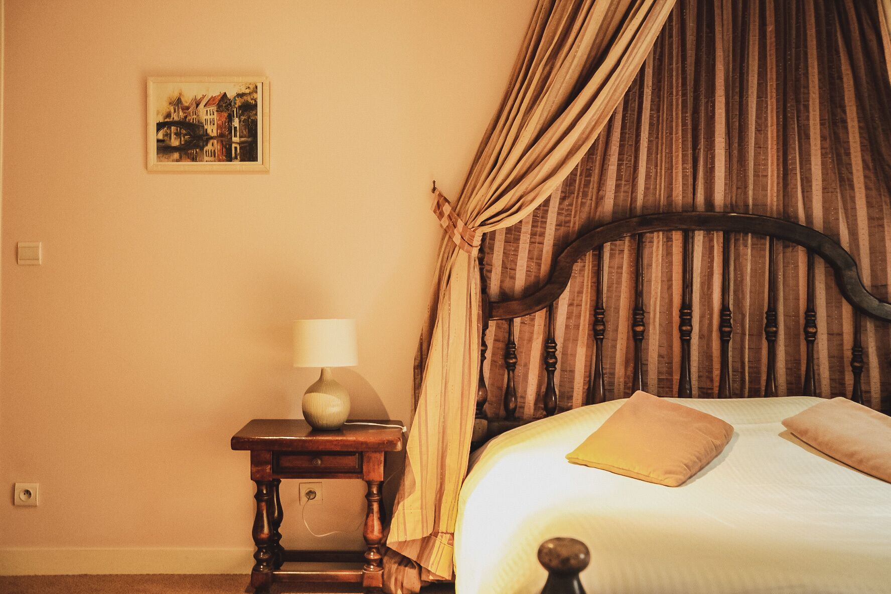 A room with a bed, a nightstand with a lamp, and a painting on the wall.