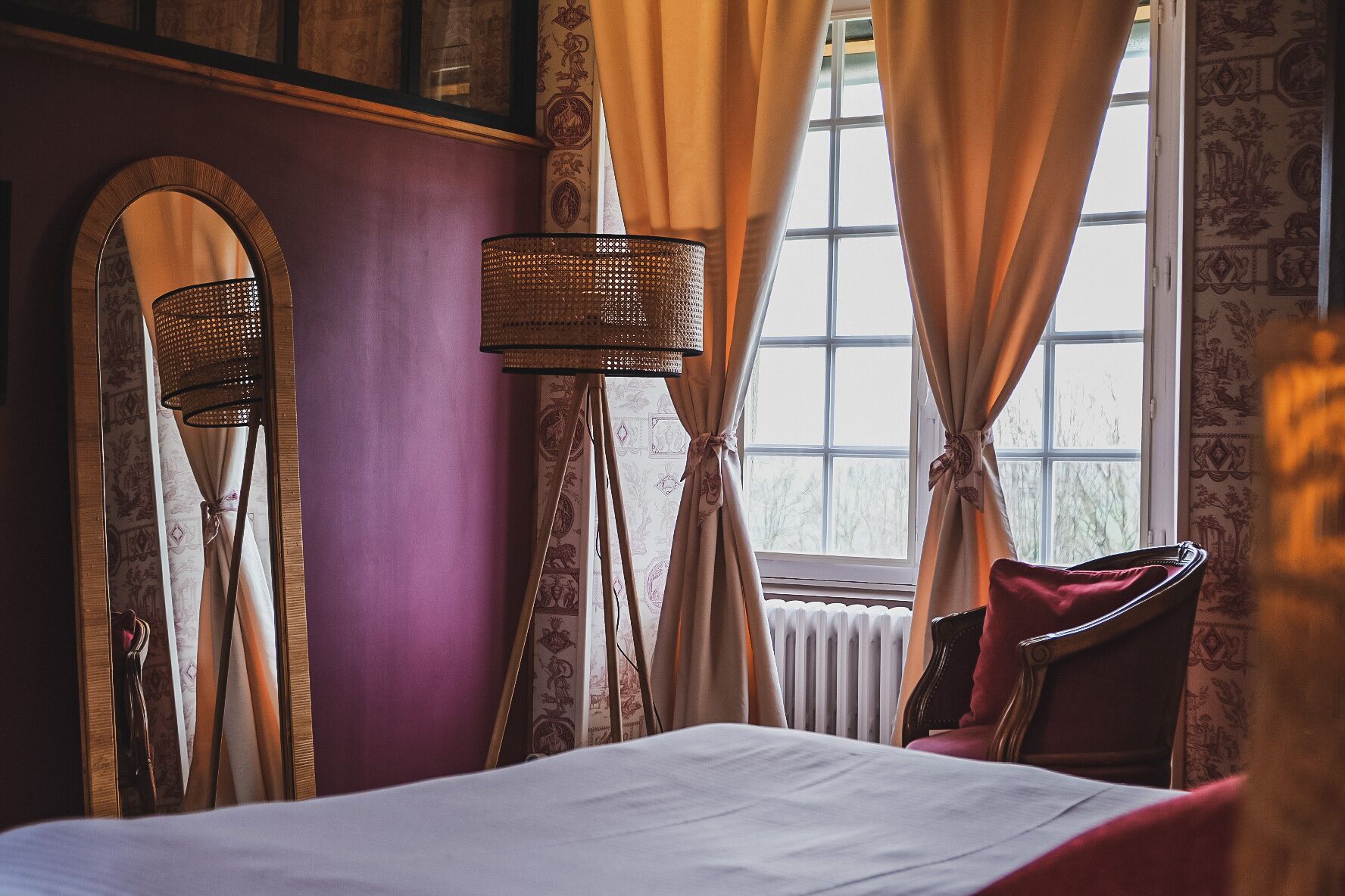 A bedroom with a bed, a mirror, a lamp, and curtains.