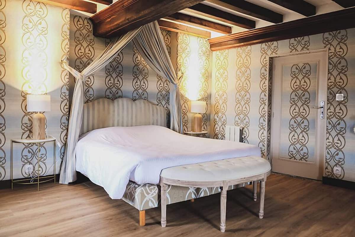 A bedroom with a canopy bed, wooden flooring, patterned wallpaper, and a door with a decorative design.