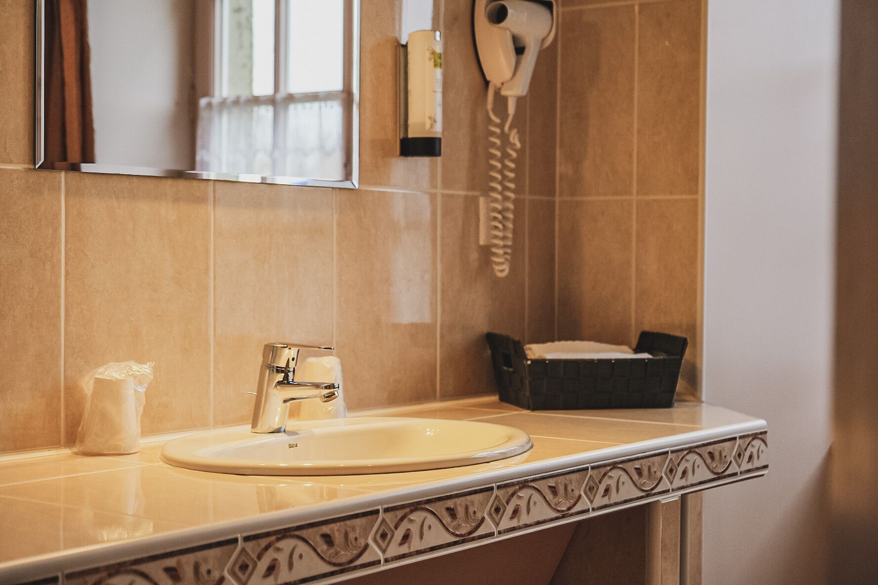 A bathroom with a sink, a mirror, a hand dryer, and a trash bin.