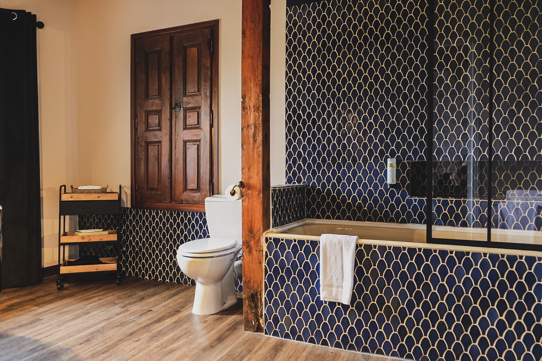 A bathroom with a toilet, wooden shelves, a towel rack, and a patterned wall.