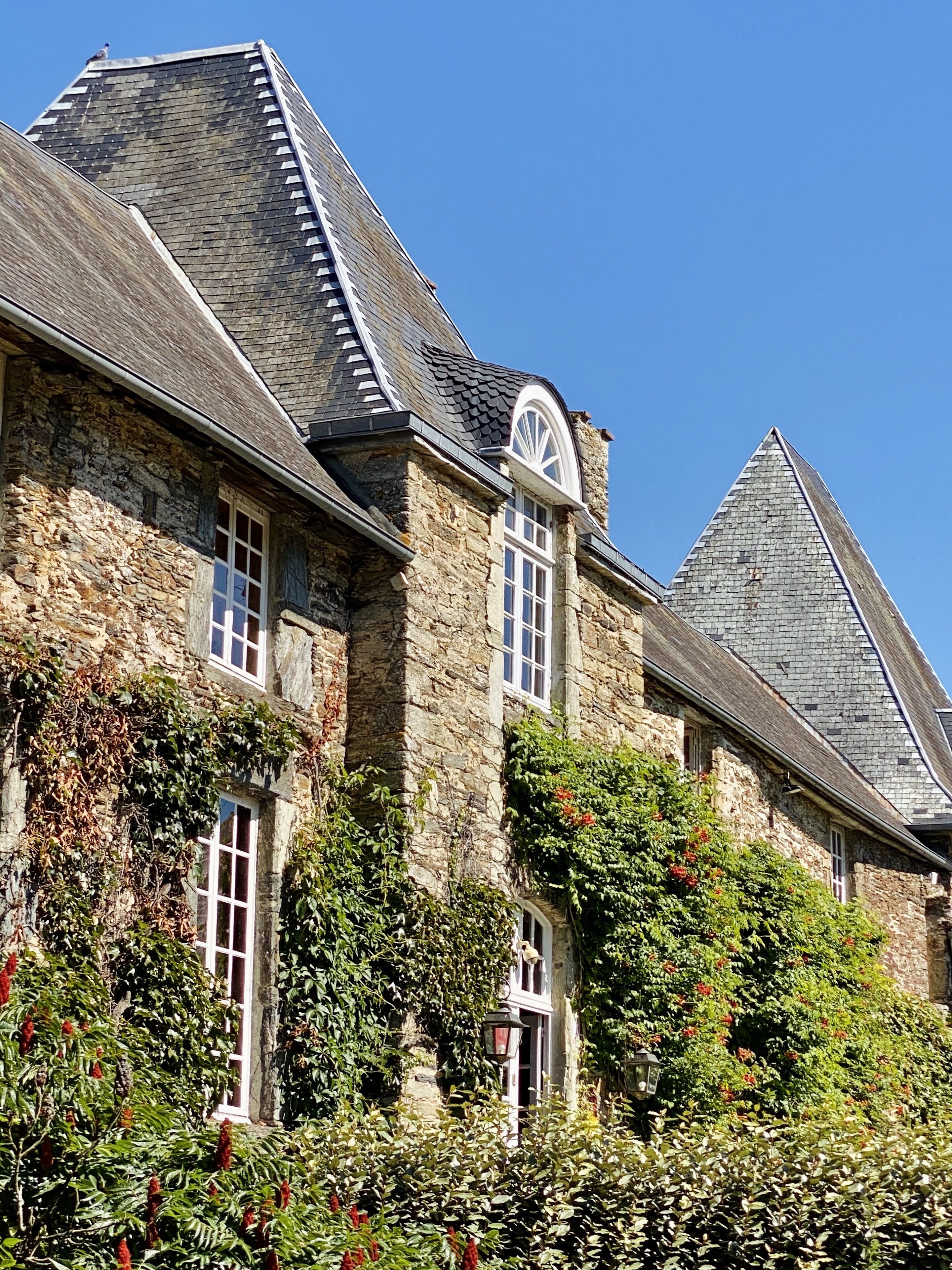 A stone building with a steeply pitched roof, large windows, and a prominent arched window.