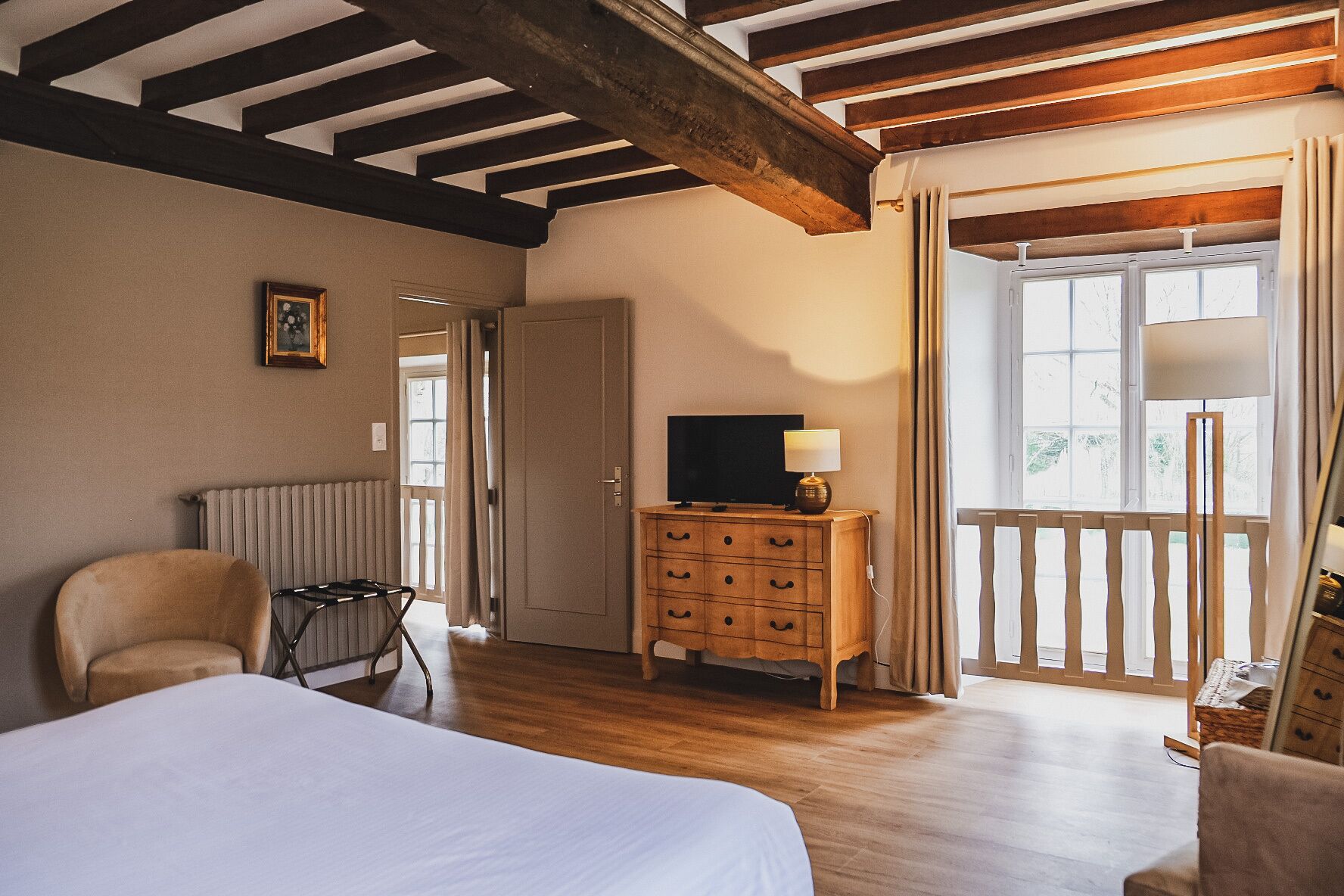 A room with a bed, a wooden dresser, a television, and a window with curtains.