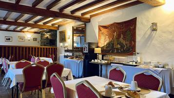 A restaurant with wooden beams, tables with white tablecloths, red upholstered chairs, and a tapestry on the wall.