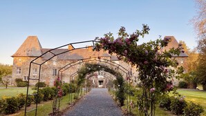 A stone building with a large archway leading to a gravel path. - Château de la Roque (Thereval)