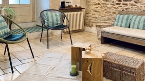 A cozy living room with a stone wall, wooden beams, wicker furniture, and hanging paper lanterns. - Château de la Roque (Thereval)