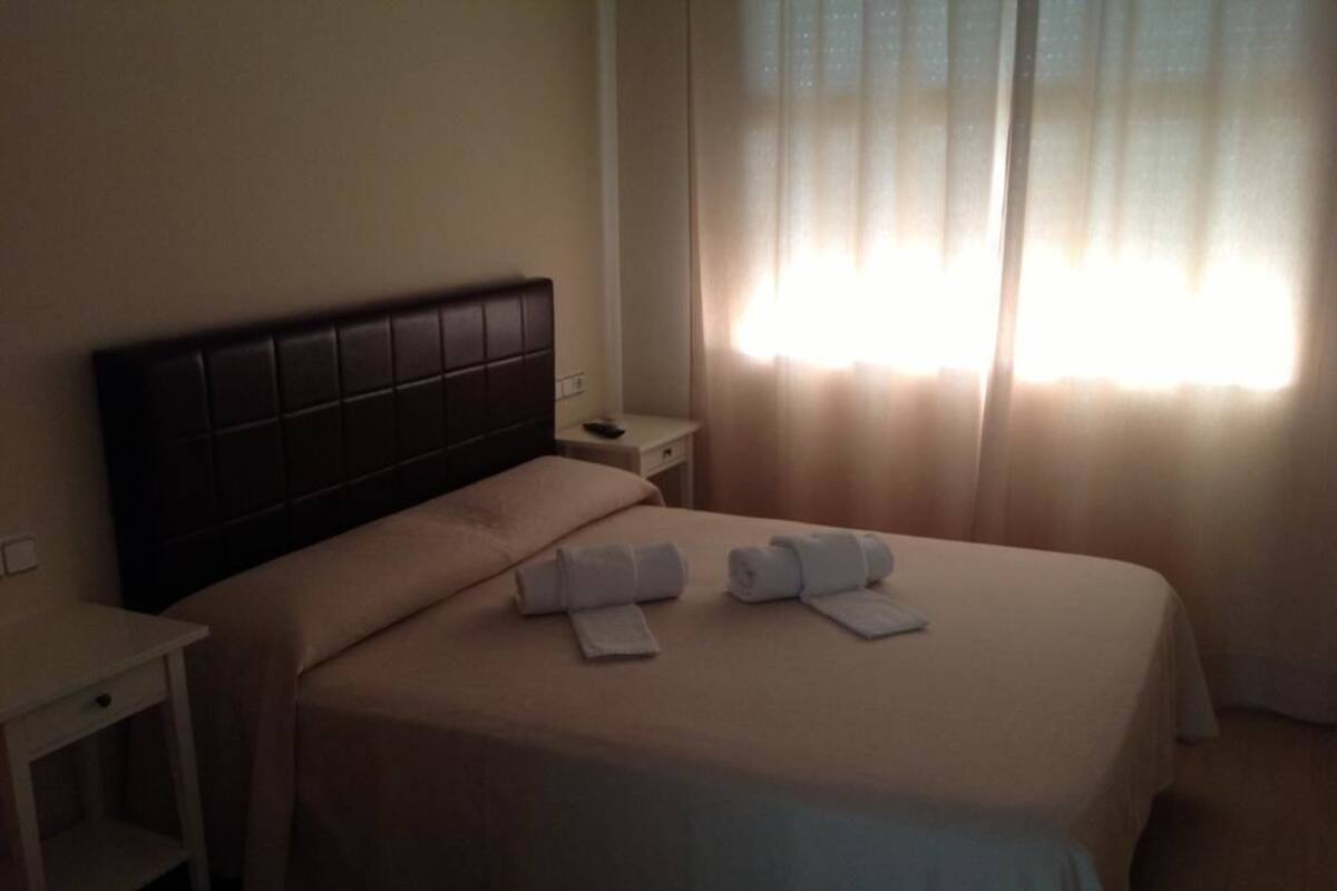Quarto de hotel com cama, mesa de cabeceira e janela com cortinas.
