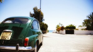 Een klassieke groene auto geparkeerd op een zonnige straat, met in de verte een heldere uitzicht op de oceaan.