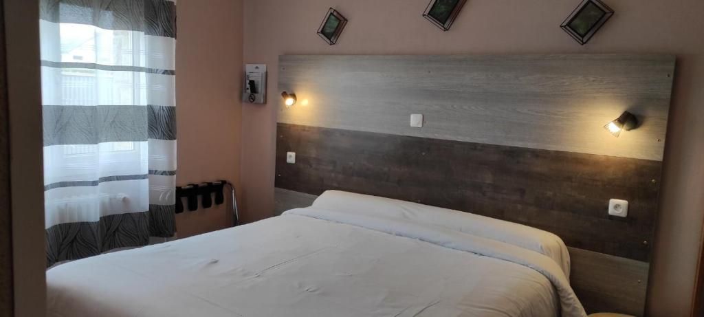 A hotel room with a bed, a headboard with wall-mounted lights, a window with a curtain, and a wall-mounted telephone.
