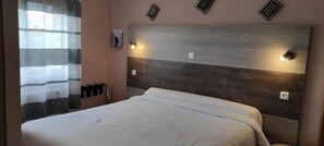 Habitación de hotel con cama, cabecera con luces empotradas en la pared, ventana con cortina y teléfono fijo en la pared.