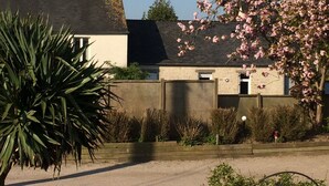 A residential building with a visible chimney, a garden with various plants, and a clear blue sky.