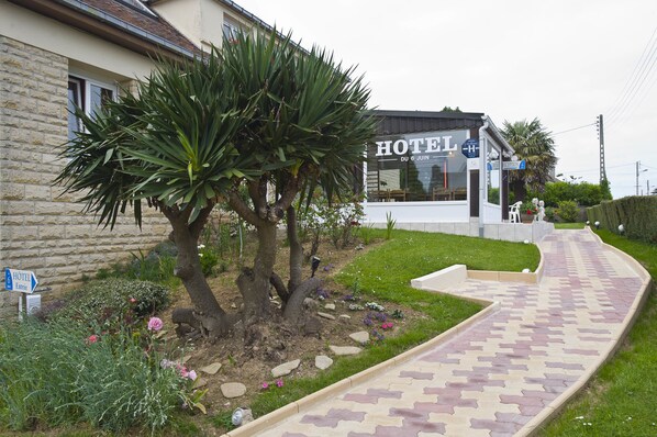 Een hotel met een geplaveid pad dat naar de ingang leidt, omringd door een tuin met diverse planten en bloemen.
