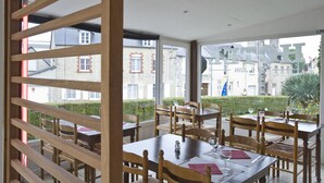 A restaurant with wooden furniture and large windows overlooking a garden and buildings.