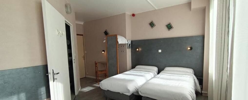 A room with two beds, a door, a mirror, and a wall-mounted light fixture.