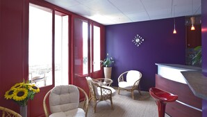 A room with a red door, large windows, wicker chairs, a small table, and a reception desk.