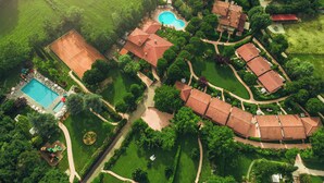 Vue aérienne d’un complexe hôtelier doté d’une piscine, d’un court de tennis et de plusieurs bâtiments aux toits recouverts de tuiles rouges.