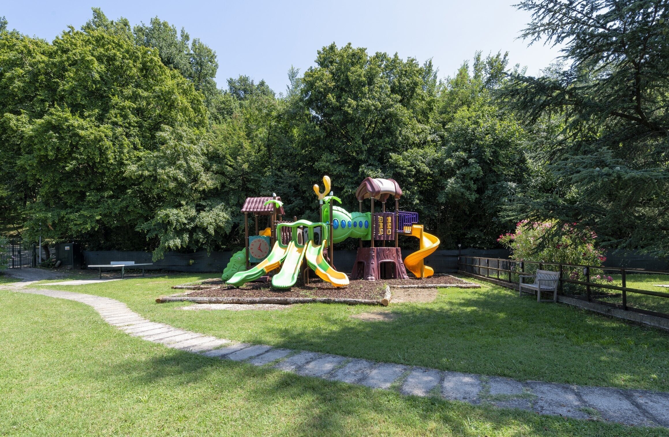 A playground with slides and climbing structures surrounded by trees.
