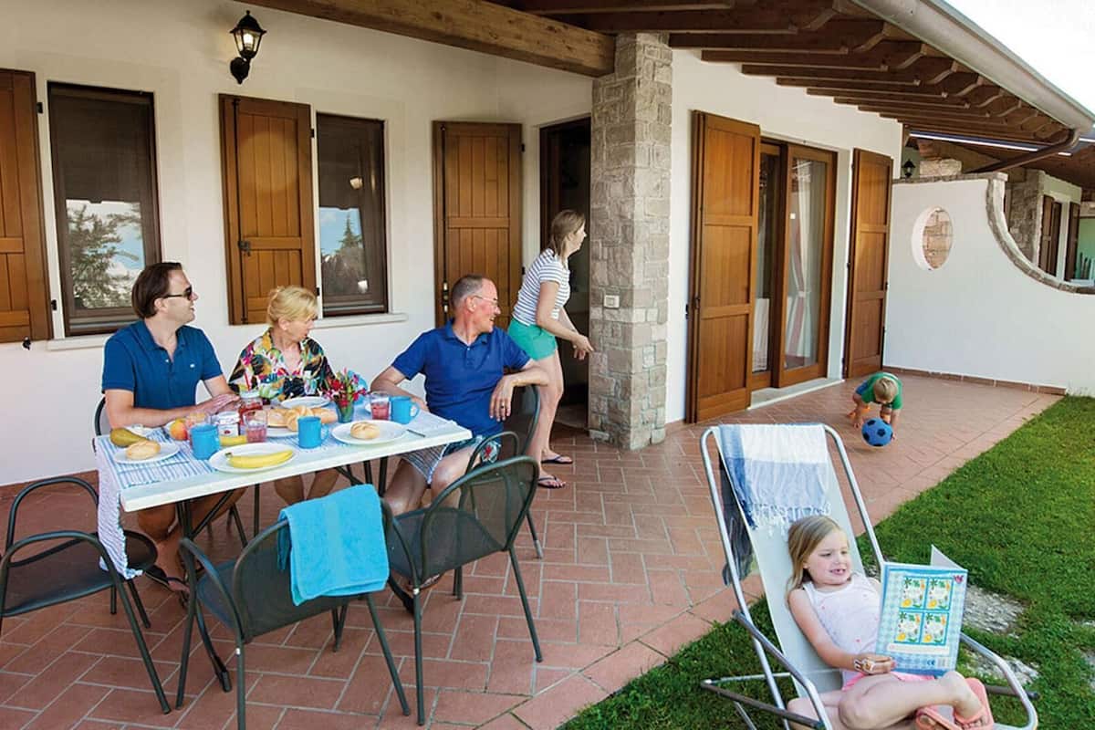 Eine Terrasse mit Tisch und Stühlen, gedeckt für eine Mahlzeit, und ein Kind, das mit einem Ball spielt.