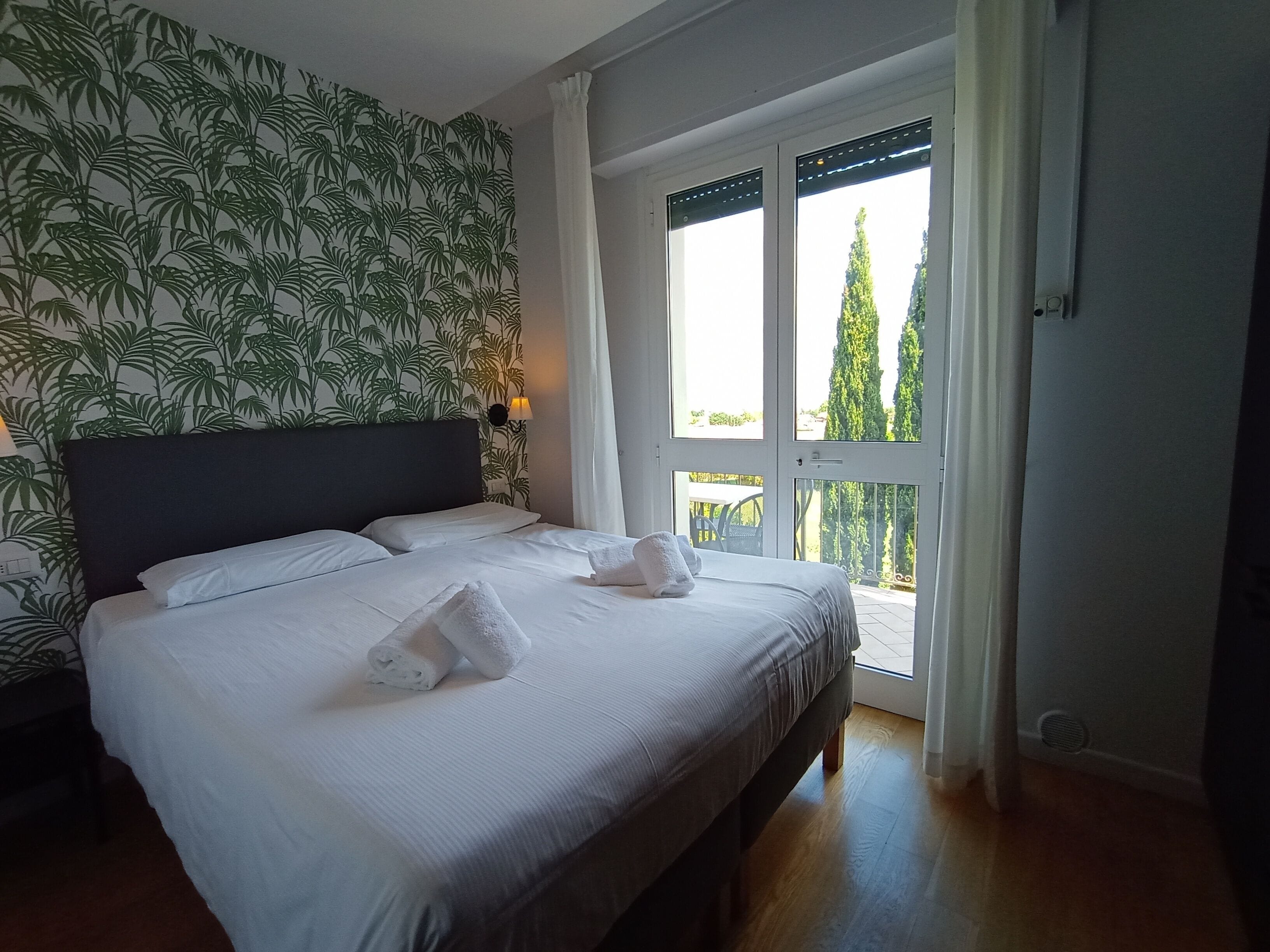 A bedroom with a bed, a headboard, a window with a view of trees, and a wall with a leaf pattern.
