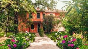 Un bâtiment rouge avec un chemin de briques menant à l’entrée, entouré d’une végétation luxuriante et de plantes en fleurs.