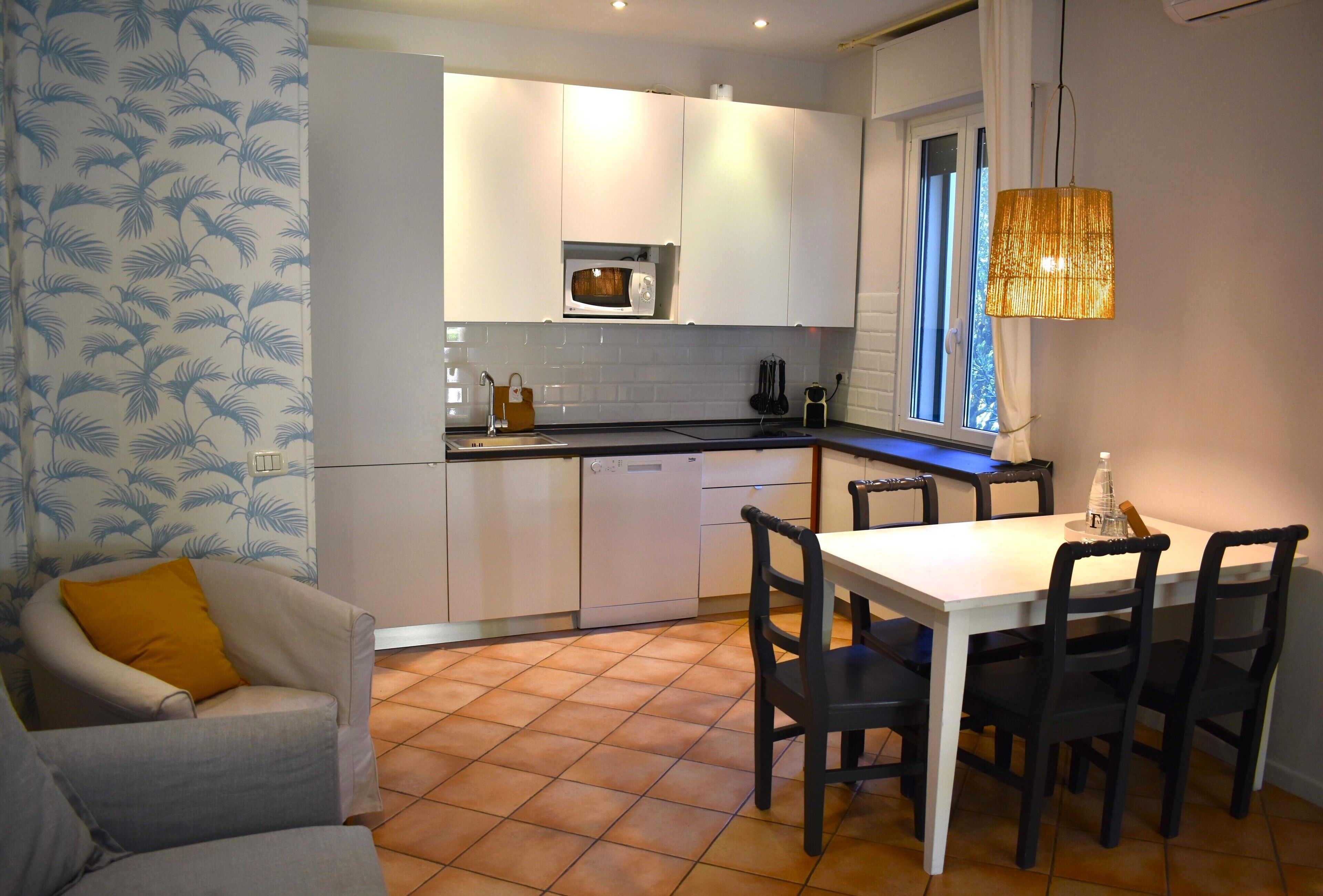 A compact kitchen with white cabinets, a microwave, a sink, and a dining area with a white table and four chairs.