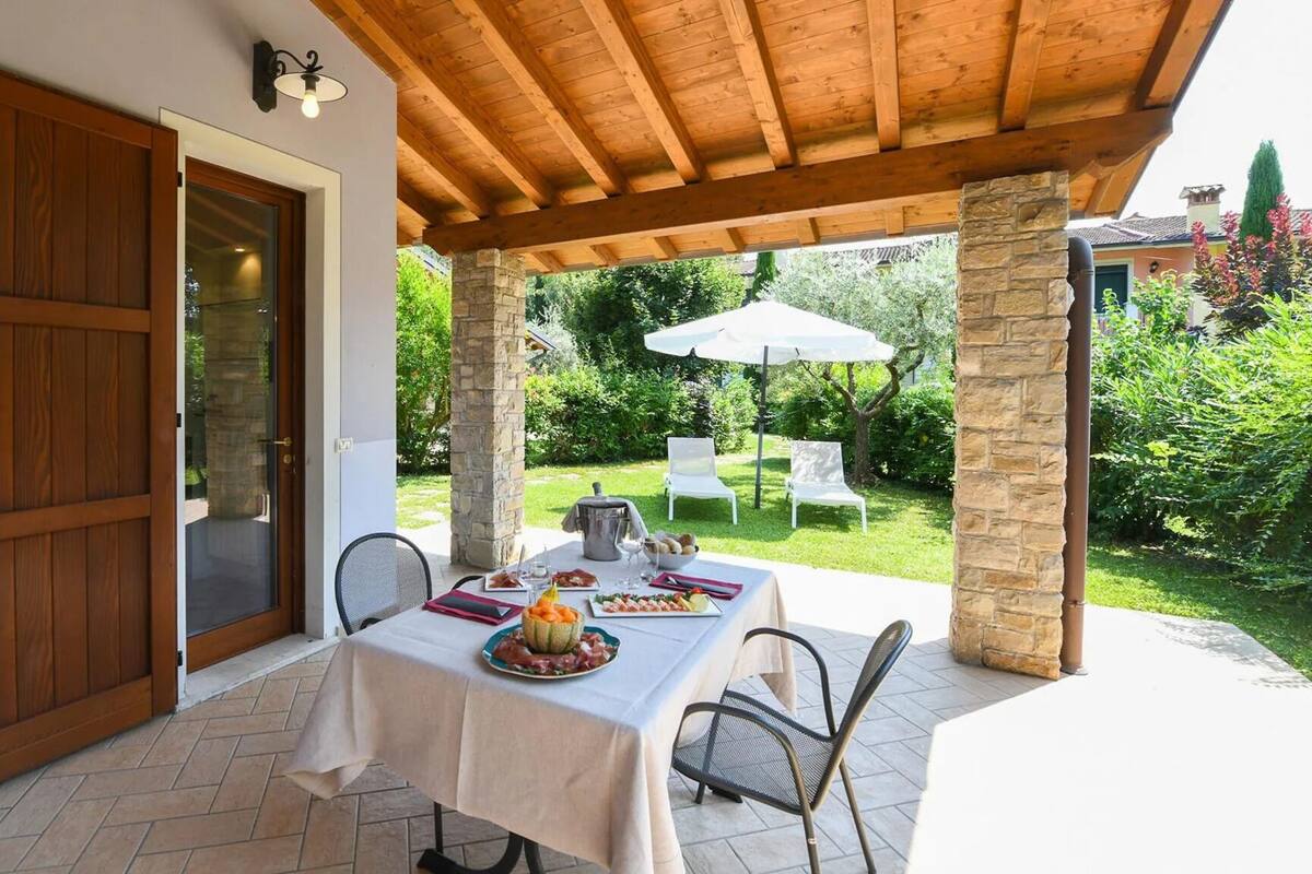 Eine überdachte Terrasse mit Esstisch, Steinsäulen und Blick auf den Garten.