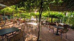 Un espace extérieur aménagé en terrasse, avec des tables et des chaises, entouré de verdure et d’arbres.