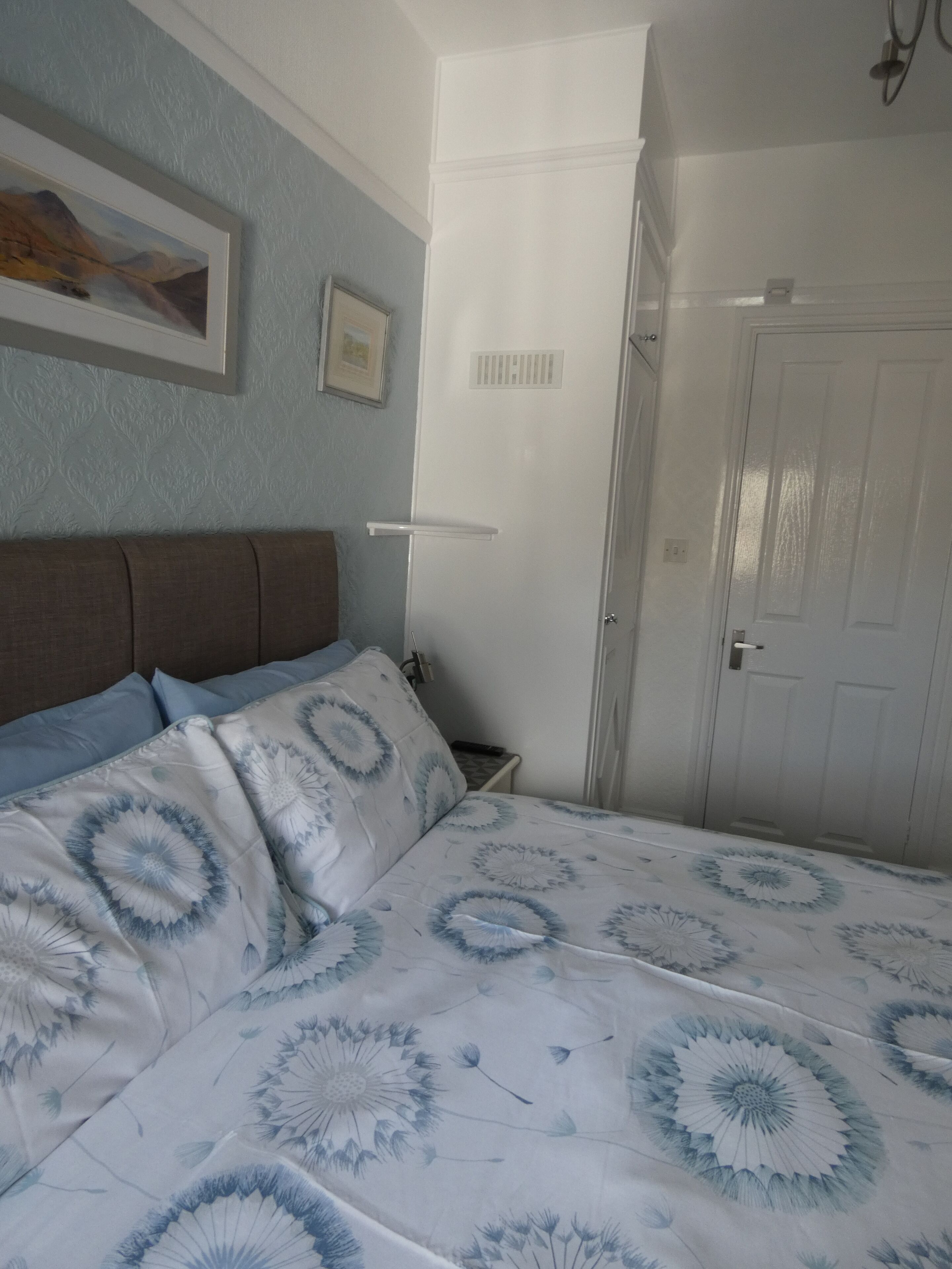 A bedroom with a bed, a nightstand, a wall-mounted shelf, and a door.
