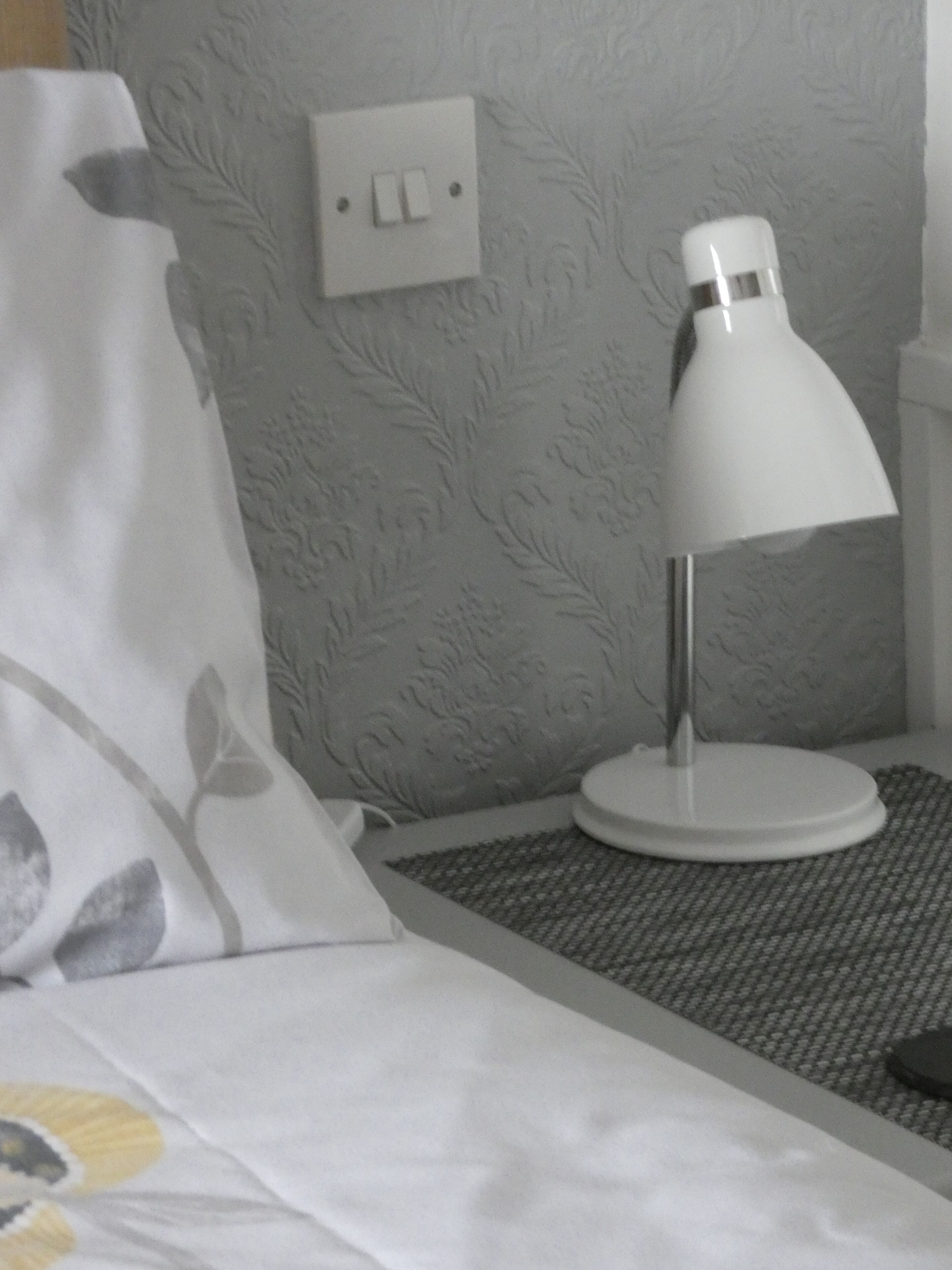 A bed with a white pillow and a white lamp on a textured gray wall.
