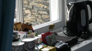 Un comptoir de cuisine avec une bouilloire, un plateau contenant divers objets et une fenêtre donnant sur un mur en pierre.