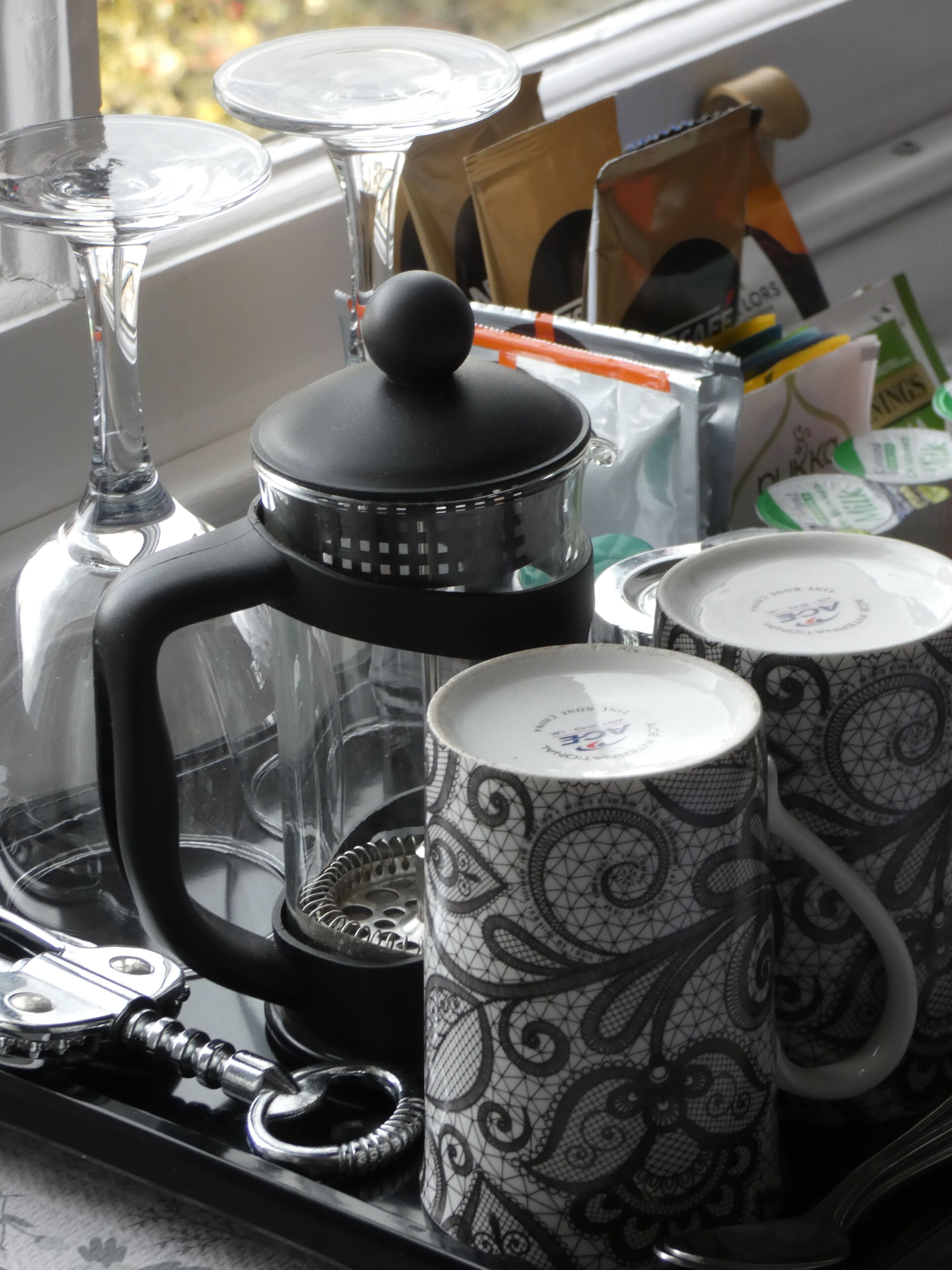 Una encimera de cocina con una cafetera, dos tazas estampadas y una jarra de vidrio.
